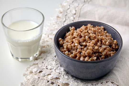 Cooked buckwheat porridge in a ceramic bowl and a glass of fresh milk on a linen tablecloth