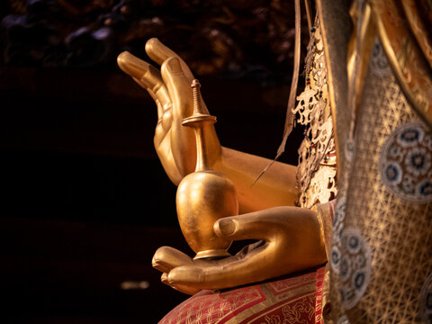 Golden Buddha statue hand holding ritual object in temple