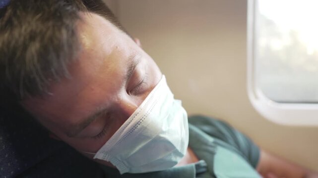 Tired sleeping train commuter wearing PPE face mask for safety. Concept travel during pandemic. Protective medical mask during the trip. Medical respiratory bandage face in transport.