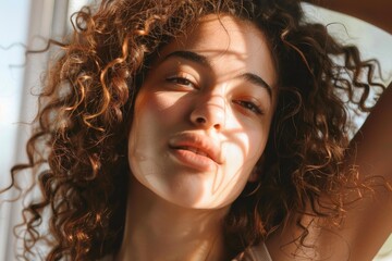 Fototapeta premium Portrait of a beautiful young woman with curly hair posing in sunlight by the window