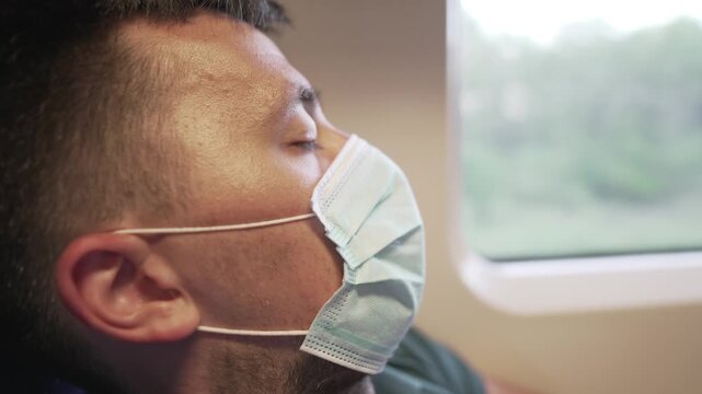 Travel safely public transport. Young man in medical mask sleeps near train window. Train passenger in protective mask on face resting. New normal travel concept. Commuter sleep covid 19, coronavirus.