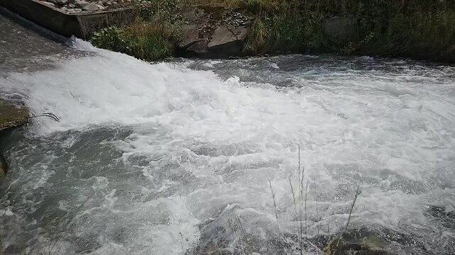 close up of fast flowing white water rushing over rocks and a small concrete dam in a rural river
