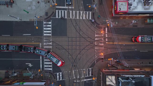 Top down showing Toronto streetcars turning left at busy intersection with traffic lights, automobiles, and pedestrians crossing street during rush hour commute