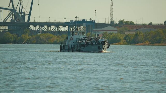 Small utility boat cruises on river against backdrop of industrial port with cranes and large bridge. Hazy daylight creates calm, working atmosphere. Muted colors and realistic style