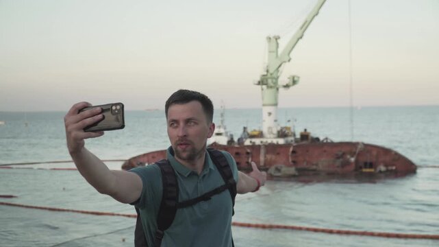 Man blogger records video blog on mobile phone for social media about accident of wreck tanker Delfi with oil in Odessa. Journalist reports on pollution of sea with oil products. Ecology problems.
