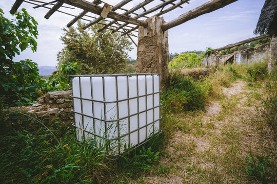 Weathered outdoor work area with caged water tank, timber beams, old stone walls, vegetation, and practical rural infrastructure in a reclaimed ruin setting