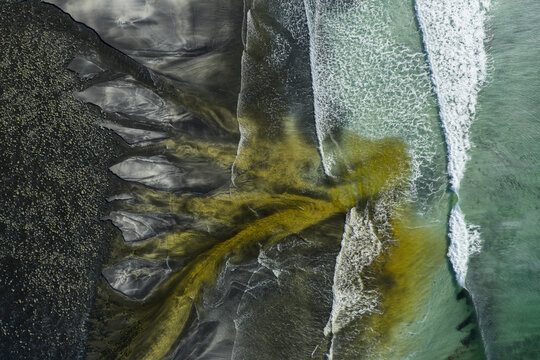 Aerial view of Talisker Bay Beach with dark volcanic sand and golden sediment flowing into turquoise waves Isle of Skye, Scotland, United Kingdom.