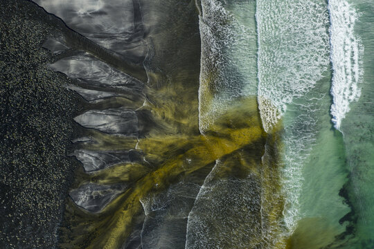 Aerial view of Talisker Bay Beach with dark volcanic sand and white waves mixing with a yellow sediment stream in the turquoise water Isle of Skye, Scotland, United Kingdom.
