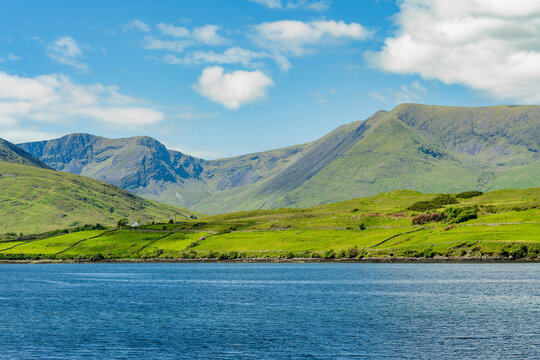 Green mountain slopes rise above Killary Fjord under bright skies in western Ireland. This image is a scenic landscape focused more on the fjord lush hillsides than the water.