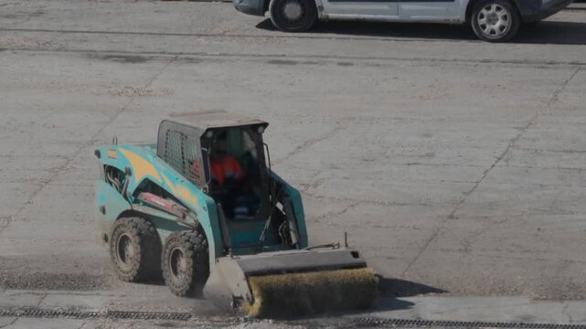 Bobcat cleans large area of gravel in construction site during daytime in the city