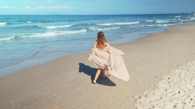 Woman running freely along the sandy beach shoreline with waves breaking, enjoying summer vacation and a leisurely escape by the ocean, captured with an aerial perspective