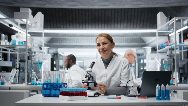 Clinical microbiologist using compound microscope for detailed cellular analysis research. Female cytotechnologist doing tissue sample examination inside modern laboratory facility, camera A