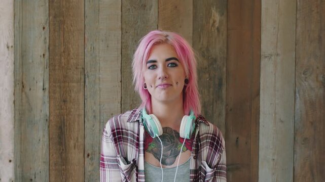 Face, woman and punk fashion with piercings, headphones and pink hair for alternative aesthetic. Creative, female person and edgy style with audio tech, tattoo and individuality on wood background.
