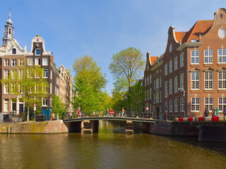 Obraz premium Scenic view of Amsterdam canal with traditional Dutch architecture, bridge and spring trees