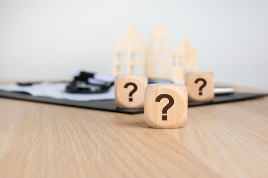 a natural wooden block printed with question mark sits sharply in the foreground on a wooden desk