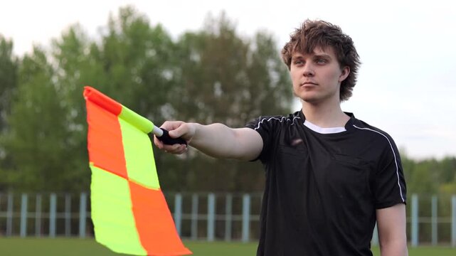 Assistant referee in black uniform holding a linesman flag on a soccer field, signaling during a match. Concept of fair play and game control in football.