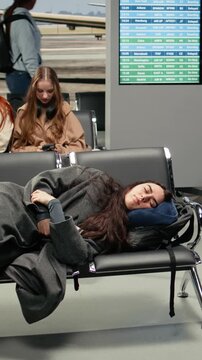 Vertical video Tired woman in airport lounge sleeping on metal bench during long airplane layover. Jet lagged traveler resting on seats, napping on neck pillow while waiting for delayed plane, camera