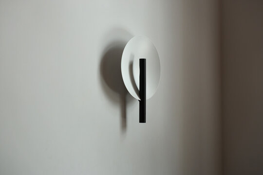 Minimal modern wall sconce with a round backplate and black cylindrical lamp casting a soft shadow on a neutral wall, ideal for contemporary interiors, ambient lighting, and minimalist decor 