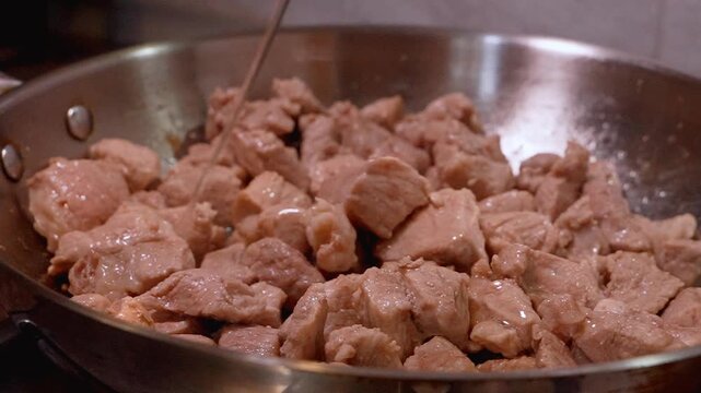Pieces of pork sizzling in a hot stainless steel pan, stirring with a wooden spatula - a delicious and simple meal, aslo is poured abundantly,