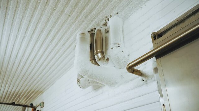 Frost-covered pipes in industrial refrigerator. Engineering technologies for maintaining preset subzero temperature and freezing processed meat product in production area of meat processing plant