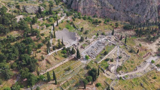 Slow aerial revealing shot of the archaeological site of Delphi, showing the ancient theatre and the temple of Apollo ruins on the slope of mount Parnassus, a famous landmark in Greece