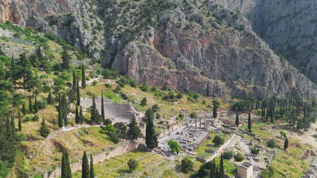 High angle aerial view of the ruins of Delphi on the slope of mount Parnassus in Greece, showing the ancient theatre, the treasury of the athenians, and the temple of Apollo on a sunny day