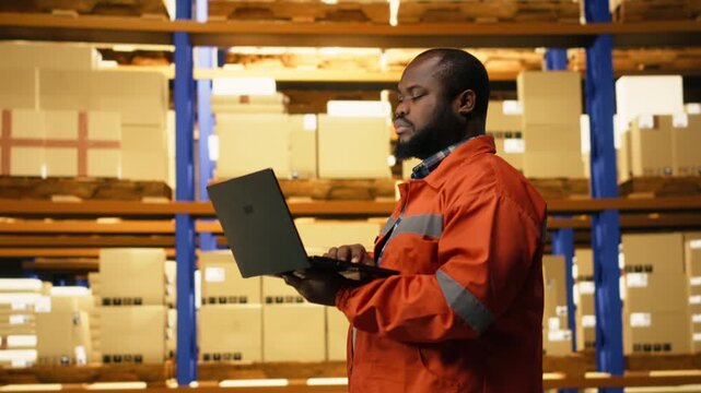 Portrait of african american worker using laptop for inventory management. Fulfillment center operations coordinate shipping and delivery, maintaining efficient supply chain workflow performance.
