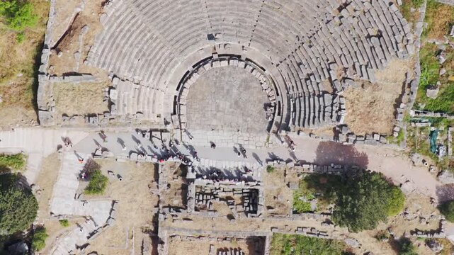 Aerial top-down view of tourists exploring the ancient greek theater ruins at Delfi, a significant archaeological site and popular historical travel destination in Greece.