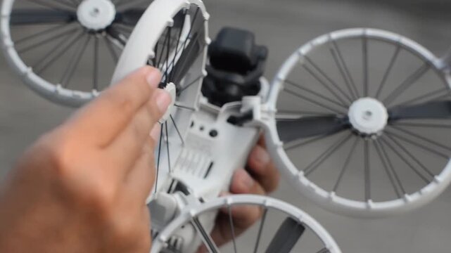 Hands unfolding the arms of a compact white drone for flight preparation.