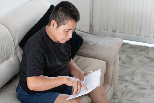 Middle-aged man reading a white notebook on the sofa, with his little finger amputated, showing his daily routine.