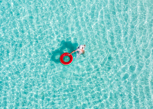 Aerial view of a person with a watermelon inflatable ring in crystal clear turquoise water Vashafaru, Haa Alif Atoll, Maldives.