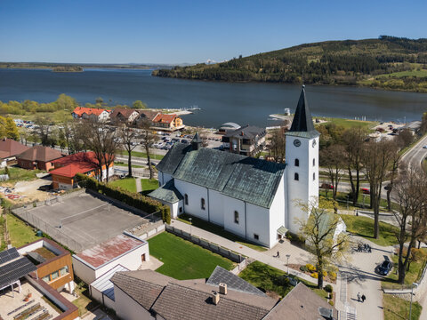 Aerial view of the Roman Catholic Church of Saints Simon and Jude with its tall steeple overlooking the Orava Reservoir and green hills in Namestovo, Zilina Region, Slovakia.
