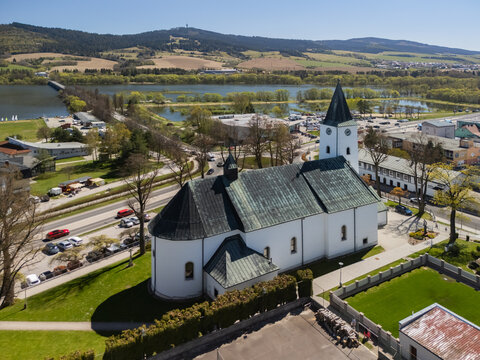 Aerial view of the Roman Catholic Church of Saints Simon and Jude with its white walls and green roof overlooking the Orava Reservoir and hills in Namestovo, Zilina Region, Slovakia.