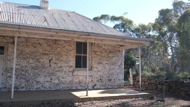 Historic bluestone cottage with corrugated iron roof and veranda at Eynesbury, Victoria, Australia; weathered stone walls of a colonial-era pioneer residence set against native eucalyptus forest.