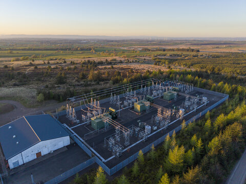 Aerial view of Eaglesham Moor electrical substation with power lines and transformers surrounded by green trees under a golden sunset sky Kilmarnock, Scotland, United Kingdom.