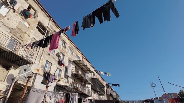 Colorful laundry hanging on clotheslines between old residential buildings in a poor urban area. The clothes are waving in the wind against a clear blue sky, illustrating daily life in a ghetto