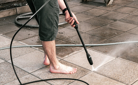 A man washes the joints of garden tiles in his yard using a kercher.