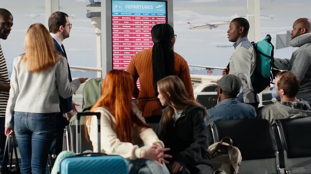 Distressed by plane delays, departure board screen and worried tourists in airport. Berating airline company, electronic schedule display and passengers alarmed by canceled flights announcement