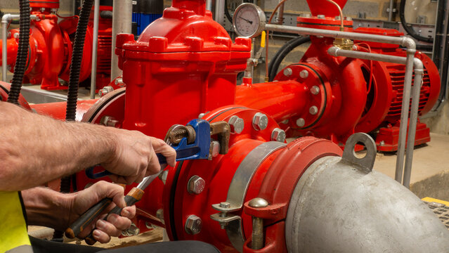 Sprinkler engineer tightening a pipe flange with spanners on a fire protection system during planned maintenance work. Essential life safety equipment planned maintenance.