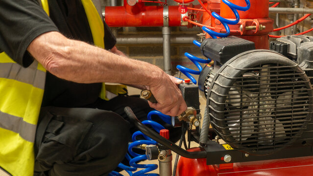 Sprinkler engineer servicing a compressor on a fire protection system during planned maintenance work. Essential life safety equipment planned maintenance.