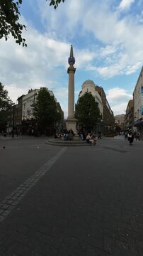 Timelapse of pedestrians walking around Seven Dials Sundial Pillar with cloudy blue sky in London, United Kingdom. Vertical video