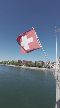 Swiss flag waving in the wind on Mittlere Br&uuml;cke bridge with the Rhine river in Basel, Switzerland. Vertical video