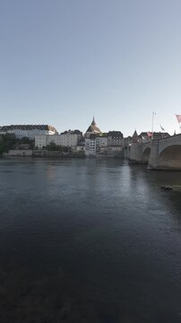 Handheld panning shot of Mittlere Br&uuml;cke bridge and old town skyline over the Rhine river at dusk in Basel, Switzerland. Vertical video