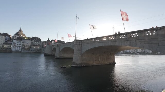 Mittlere Br&uuml;cke bridge with Swiss flags over the Rhine river and old town skyline at golden hour in Basel, Switzerland