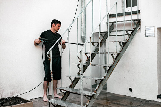 An adult boy washes the railings of a garden staircase using a kercher.
