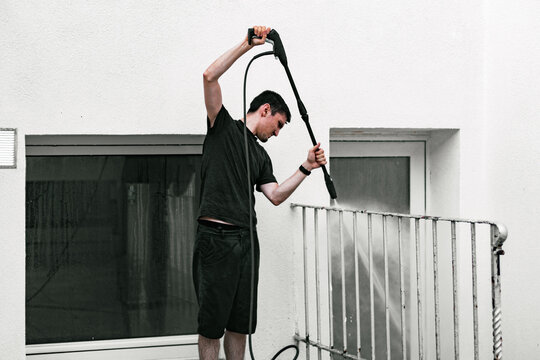 A boy washes metal railings in a courtyard using a kercher.