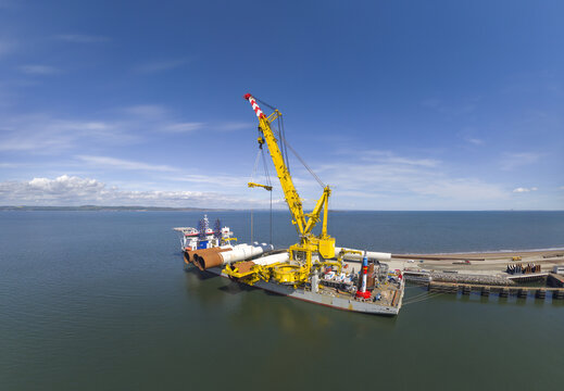Aerial view of a large yellow crane ship loading wind turbine components at the Port of Leith under a clear blue sky Edinburgh, Scotland, United Kingdom.