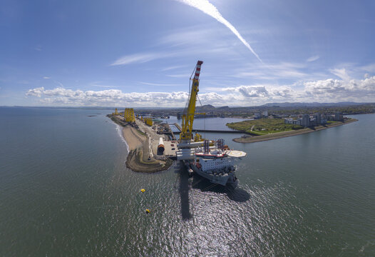 Aerial view of the industrial port of Leith featuring a large yellow crane and a docked ship under a clear blue sky in Edinburgh, Scotland, United Kingdom.