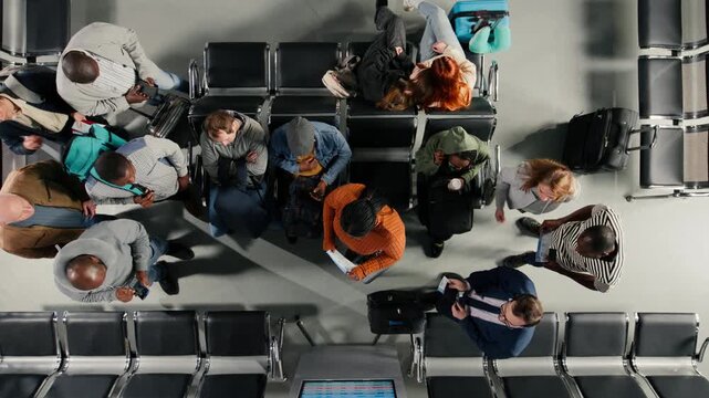 Distressed by plane delays, departure board and top down view of troubled tourists in airport. Upset by canceled flights, announcements on FIDS display and high angle shot of passengers