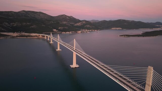 High-angle perspective of Peljesac Bridge over the Adriatic Sea during twilight. Professional drone photography of Croatia's landmark infrastructure at golden hour.